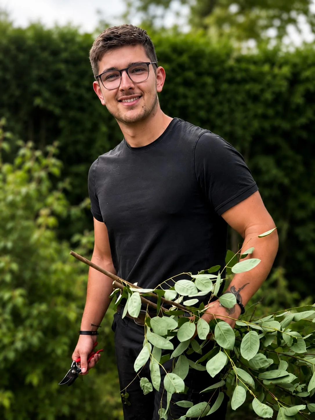 Paul Hermann Paschkewitz, Inhaber von Paul Hermann Gartenbau und Outdoor Living, mit Gartenschere und frischem Grünschnitt vor einer Hecke in Elmshorn